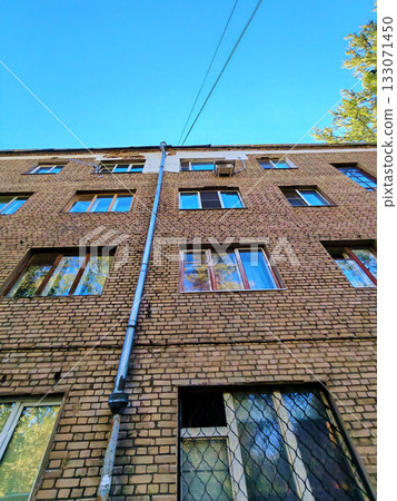 Upward view of an old brick apartment facade with a long metal downpipe, patch repairs near the roof and an external AC unit. Useful for content about brick repointing, drainage replacement, window 133071450