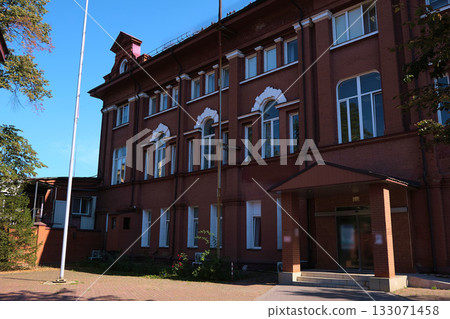Street view of a historic red brick institutional building with arched windows, white keystones and a small entrance canopy in even daylight. Relevant for ads about masonry restoration, facade 133071458