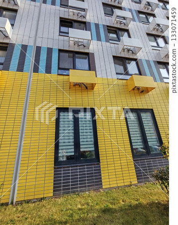 modern high-rise residential complex with yellow and white facades, set against a clear sky. The structure reflects contemporary urban living, featuring geometric design elements and ample parking 133071459