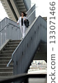 A confident woman in white sportswear walks down an urban staircase, holding Kangoo Jumps shoes. The structured lines of the stairs frame the subject, symbolizing progress and movement. 133071466