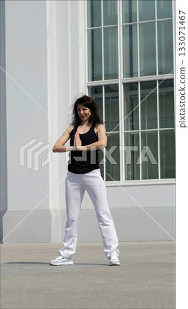 A woman in sportswear stands outdoors in a yoga pose, palms pressed together in a moment of focus. The combination of fitness and modern architecture highlights the balance between movement and A woman in sportswear stands outdoors in a yoga pose, palms pressed together in a moment of focus. The combination of fitness and modern architecture highlights the balance between movement and 133071467