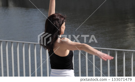 A woman does her morning warm-up by the water, combining sports and nature. The shot inspires an active lifestyle and self-care. 133071479