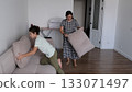 A woman and her son clean up the room, arranging soft cushions with calm focus in minimalist space. Such collaboration fosters respect, care, and good habits important for emotional growth. 133071497