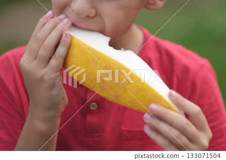 he texture of the melon is vivid as a young boy savors it, his enjoyment evident in his expression. Emphasizes the delight of simple, wholesome eating. 133071504