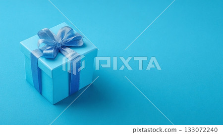 A small, sky-blue gift box, tied with a matching ribbon and bow, sits diagonally on a vibrant blue surface.  A shadow adds depth.  Perfect for a celebration or special occasion. 133072240