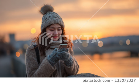 Smiling at Dusk | A woman enjoying her smartphone by the river in winter Smiling at Dusk | A woman enjoying her smartphone by the river in winter 133072327