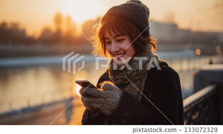 Smiling at Dusk | A woman enjoying her smartphone by the river in winter Smiling at Dusk | A woman enjoying her smartphone by the river in winter 133072329