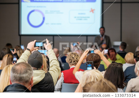Audience at a conference listening to a speaker during a presentation with a large screen 133073314