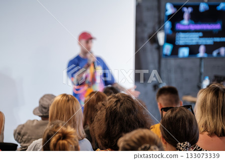 Speaker presenting to engaged audience at conference with large screen and colorful background Speaker presenting to engaged audience at conference with large screen and colorful background 133073339