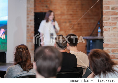 Speaker on stage delivers presentation to attentive audience in brick venue 133073340