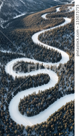 Drone aerial of winding groomed ski run cutting through dark evergreen forest high mountain winter resort Drone aerial of winding groomed ski run cutting through dark evergreen forest high mountain winter resort 133073755