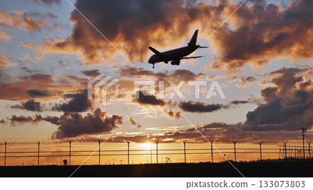 Passenger airplane landing at sunset over airport fence 133073803