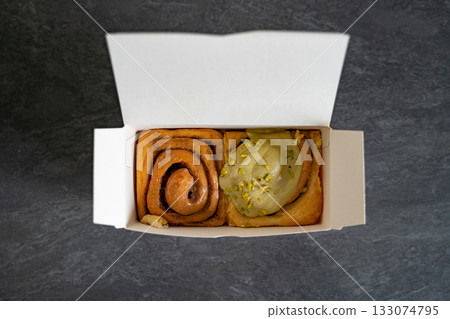 Classic and pistachio cinnamon rolls arranged in a takeout cardboard box, viewed from above. Concept of bakery, pastry, takeaway, breakfast, indulgence. Classic and pistachio cinnamon rolls arranged in a takeout cardboard box, viewed from above. Concept of bakery, pastry, takeaway, breakfast, indulgence. 133074795