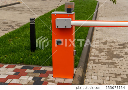 A bright orange security barrier controls access to a parking lot surrounded by green grass and pavement on a sunny day 133075134
