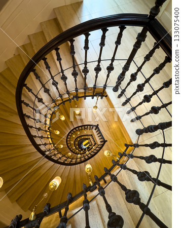 Spiral staircase with ornate iron railing and warm lights viewed from above Spiral staircase with ornate iron railing and warm lights viewed from above 133075400
