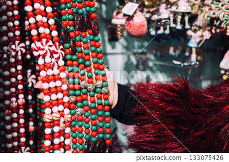 Close-up of a shoppers hand touching Christmas candy garlands in a festive retail display. Tactile holiday shopping, product interaction, festive merchandising, ornament detail focus 133075426