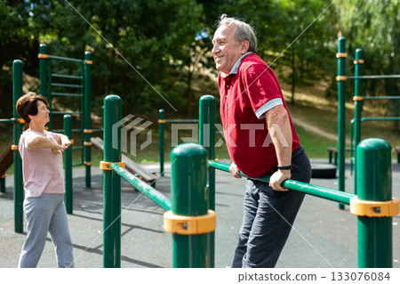 Senior man pulls up on crossbar in city park on sports ground Senior man pulls up on crossbar in city park on sports ground 133076084