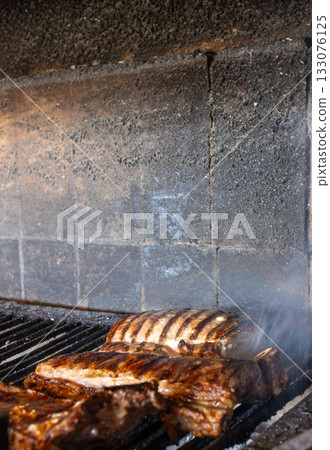 Pork ribs grilling over hot coals on an authentic argentine barbecue, showing flavorful meat cooking with rising smoke, perfect for a traditional outdoor meal Pork ribs grilling over hot coals on an authentic argentine barbecue, showing flavorful meat cooking with rising smoke, perfect for a traditional outdoor meal 133076125
