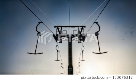 Ski lift towers and cables silhouetted against dramatic winter sky low angle industrial alpine infrastructure  133076312