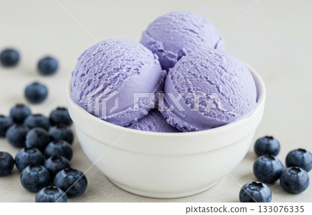 Close-up of a white bowl filled with three scoops of blueberry ice cream, garnished with a blueberry berries. Close-up of a white bowl filled with three scoops of blueberry ice cream, garnished with a blueberry berries. 133076335