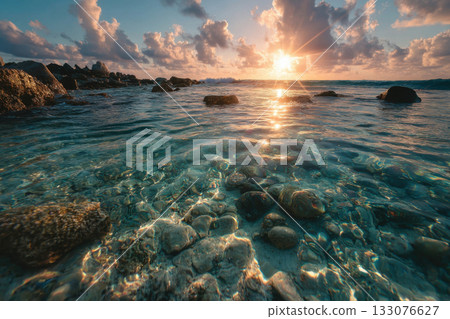 The rocky seabed is visible through the crystal-clear water at sunset. 133076627