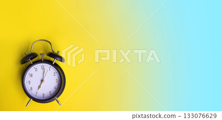 Black alarm clock on a yellow and blue empty background. Minimalist composition with copy space and bright contrasting colors.  133076629