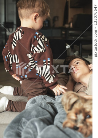 A small child is talking to his sick teenage brother who is lying in bed under a blanket. The scene shows care, empathy, and family support during illness. A touching and emotional moment illustrating 133076647