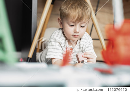 A cute two-year-old boy is playing happily in a bright, cozy room. The toddler is full of energy and curiosity, enjoying imaginative play and discovering new things. Perfect image for illustrating A cute two-year-old boy is playing happily in a bright, cozy room. The toddler is full of energy and curiosity, enjoying imaginative play and discovering new things. Perfect image for illustrating 133076650