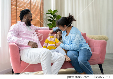 Happiness family moment on cozy pink sofa as a mother gently soothes daughter while the father smiles warmly in living room at home 133077087