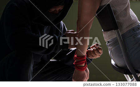 Criminal tying woman hands with red rope during hostage situation in dark room Criminal tying woman hands with red rope during hostage situation in dark room 133077088