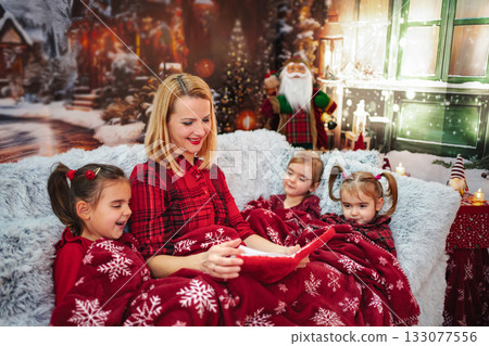 Mother reading Christmas story to children on cozy sofa 133077556