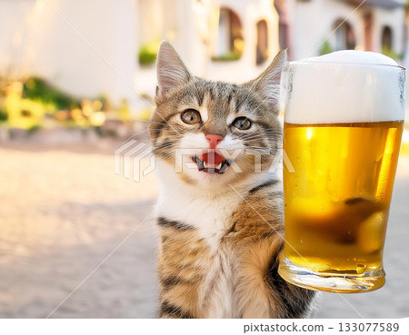 Cheers with the biggest smile! A comical photo of a happy kitten holding up a beer mug 133077589