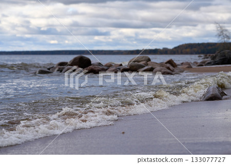 Sea waves splashing near rocks on sandy coast under cloudy autumn sky. Sea waves splashing near rocks on sandy coast under cloudy autumn sky. 133077727