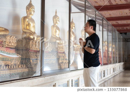 A man pays respect to the golden Buddha statues inside a temple, representing the cultural beauty of faith and traditional Thai spirituality. A man pays respect to the golden Buddha statues inside a temple, representing the cultural beauty of faith and traditional Thai spirituality. 133077868