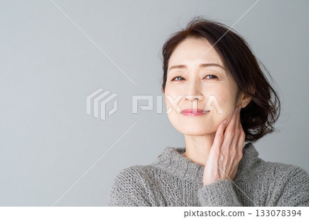 中年女性抗老照護：她面帶微笑，用手輕撫臉頰，檢查皮膚緊緻度。 133078394