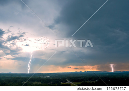 Dramatic lightning strikes illuminate stormy sky over mountains at dusk 133078717