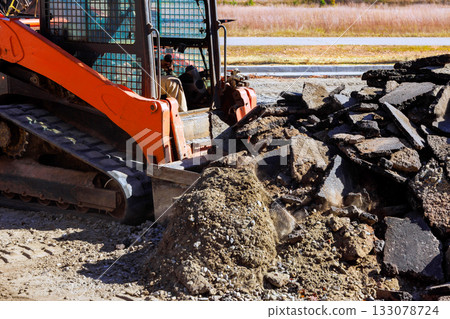 Construction equipment working on site with piles of broken asphalt debris Construction equipment working on site with piles of broken asphalt debris 133078724