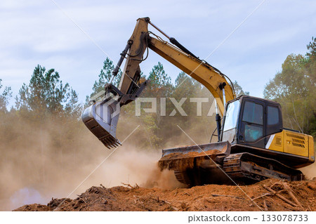 Excavator working on construction site clearing land for development in forested area Excavator working on construction site clearing land for development in forested area 133078733
