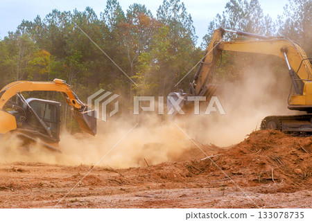 Excavators working on land clearing project in autumn landscape with dust clouds rising 133078735