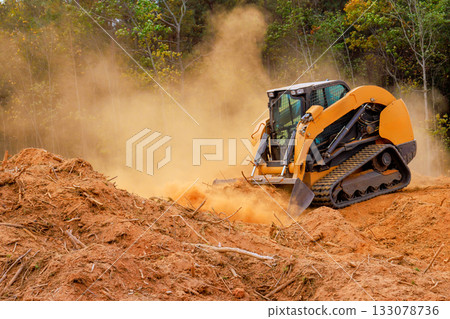 Heavy machinery clears land in forested area with visible dust dirt clouds 133078736