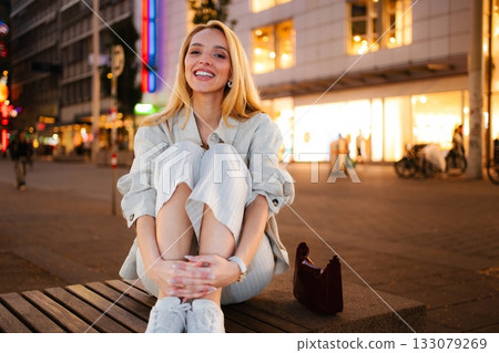 Happy young woman sitting on bench in Vienna at night Happy young woman sitting on bench in Vienna at night 133079269