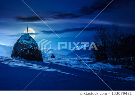 rural scenery with haystack in winter at night. countryside landscape with snow covered hill in mountains in full moon light. low angle view with snowy peak in the background. background for rural scenery with haystack in winter at night. countryside landscape with snow covered hill in mountains in full moon light. low angle view with snowy peak in the background. background for 133079481