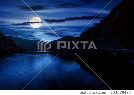mountainous landscape with lake in autumn at night. forest on hills near the shore of river under dark sky in full moon light. beautiful view of stunning place mountainous landscape with lake in autumn at night. forest on hills near the shore of river under dark sky in full moon light. beautiful view of stunning place 133079483