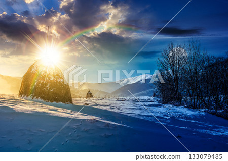 rural scenery with haystack in winter. day and night time change concept. countryside landscape with snow covered hill in mountains with sun and moon at twilight. low angle view with snowy peak in the 133079485