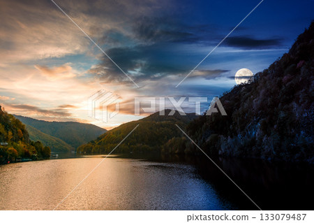 mountainous landscape with lake on autumn equinox. day and night time change concept. forest on hills near the shore of river under sky with moon at twilight. beautiful view of stunning place 133079487