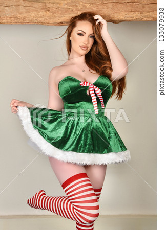 Beautiful, tall, shapely redhead model dressed as a Sexy Santa and Elf, posing against a wall in an old house 133079938