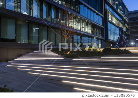 An evening view of a business center with modern glass and steel architecture and a square with a flowerbed next to it. An evening view of a business center with modern glass and steel architecture and a square with a flowerbed next to it. 133080576