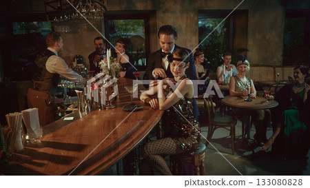 Laughing guests in vintage fashion enjoying cocktails and social moments at the bar 133080828