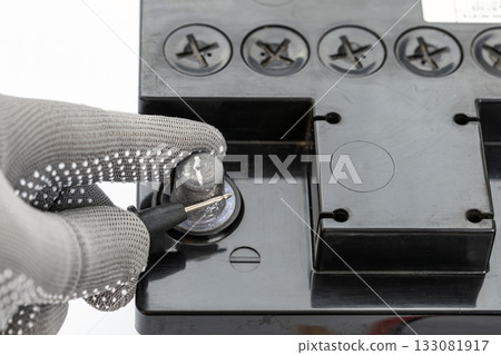 Gloved hand measures negative terminal of a black car battery with a black probe for safety. 133081917