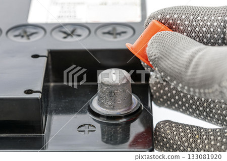 Gloved Hand Removing Orange Cap from Car Battery Terminal 133081920